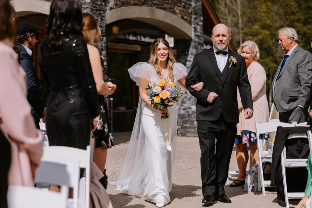 Bride walking down the aisle with her father during an outdoor wedding ceremony at Silvertip Resort in Canmore, Alberta
