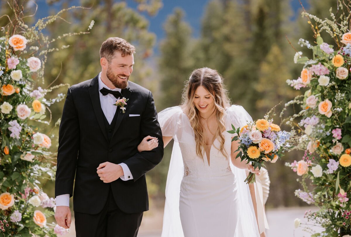 Bride and groom walking through floral ceremony pillars at a Silvertip Resort wedding in Canmore, Alberta